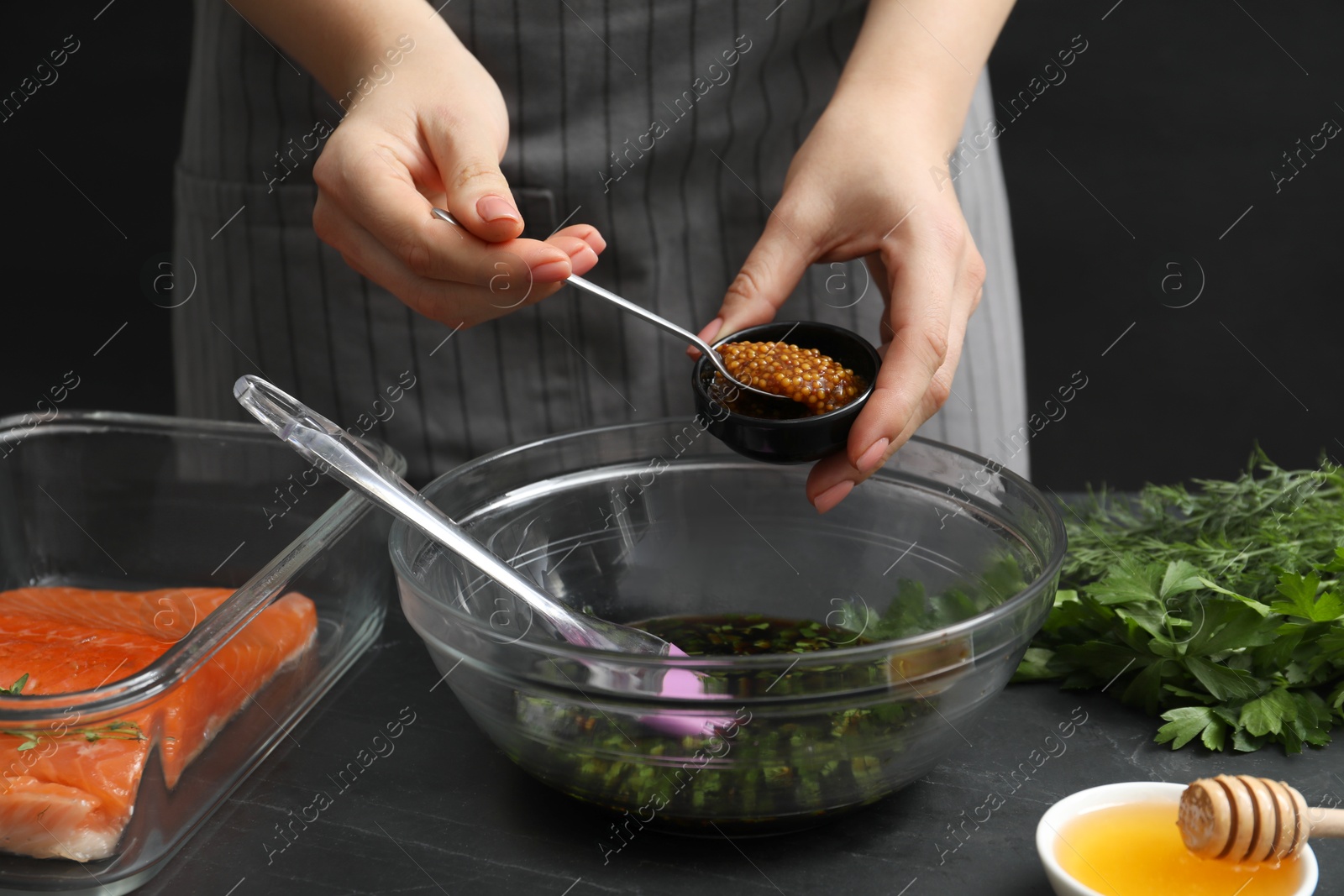 Photo of Woman adding mustard into bowl with soy marinade at dark gray table, closeup