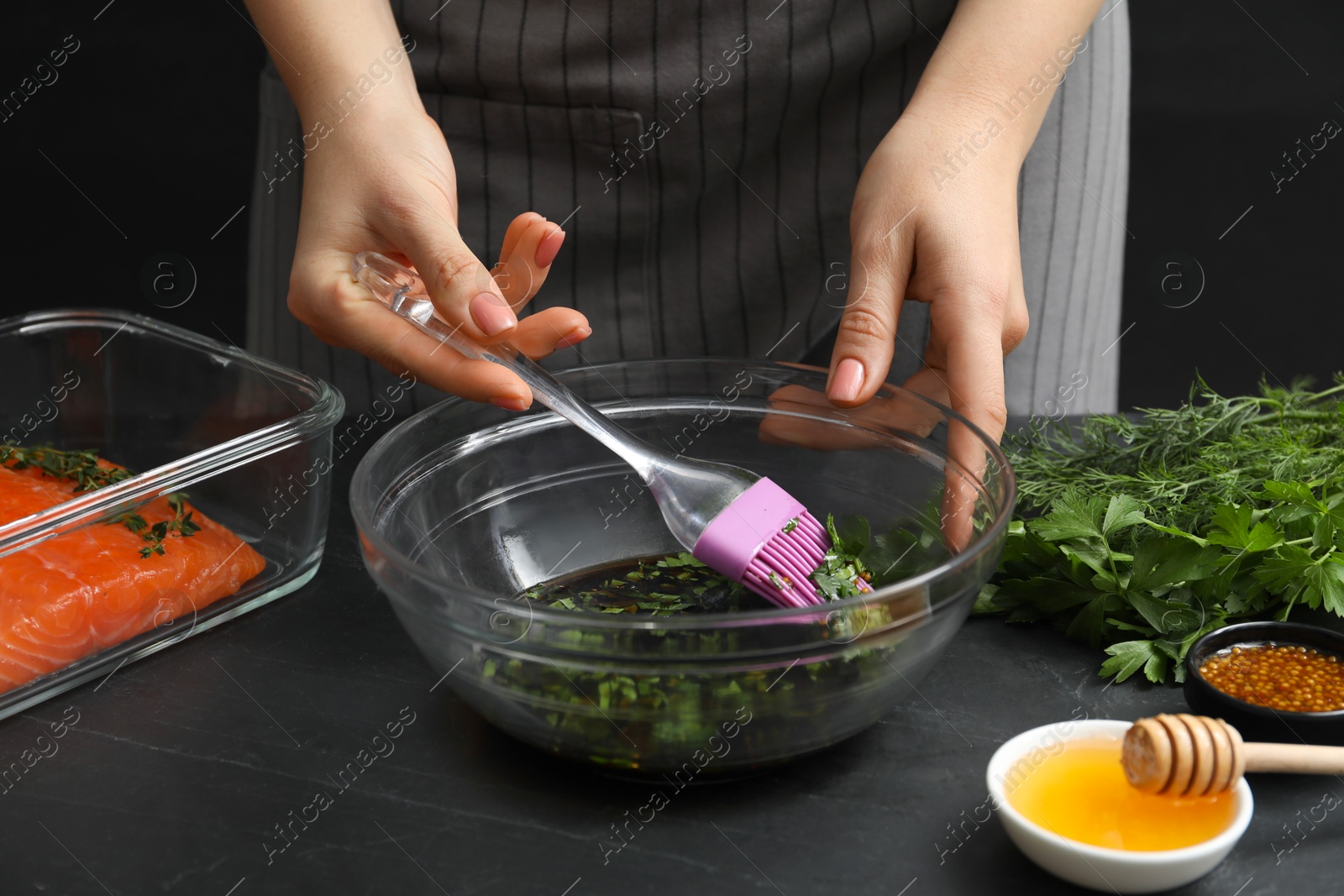 Photo of Woman making soy marinade for salmon fillet at dark gray textured table, closeup