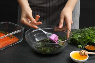 Photo of Woman making soy marinade for salmon fillet at dark gray textured table, closeup