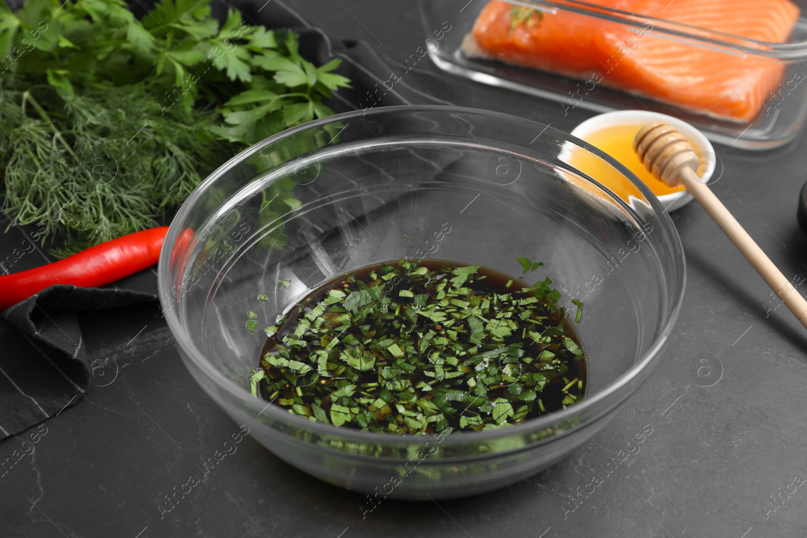 Photo of Soy marinade in bowl, salmon fillet and other products on dark gray textured table, closeup