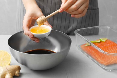 Photo of Woman adding honey into bowl with soy sauce at gray table, closeup