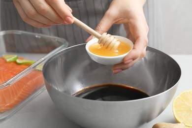 Photo of Woman adding honey into bowl with soy sauce at gray table, closeup