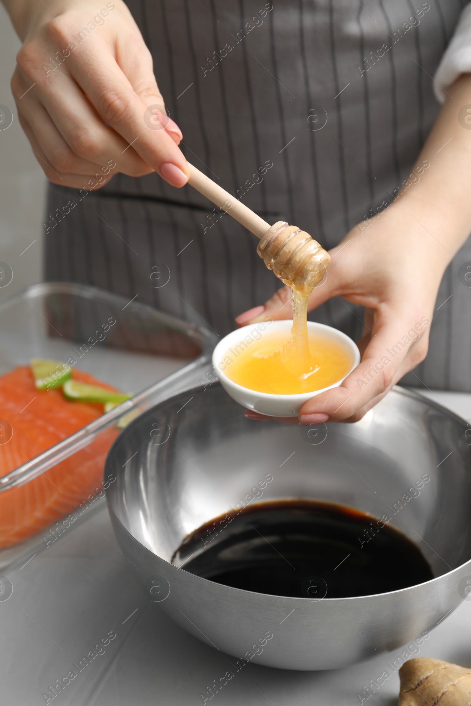 Photo of Woman adding honey into bowl with soy sauce at gray table, closeup