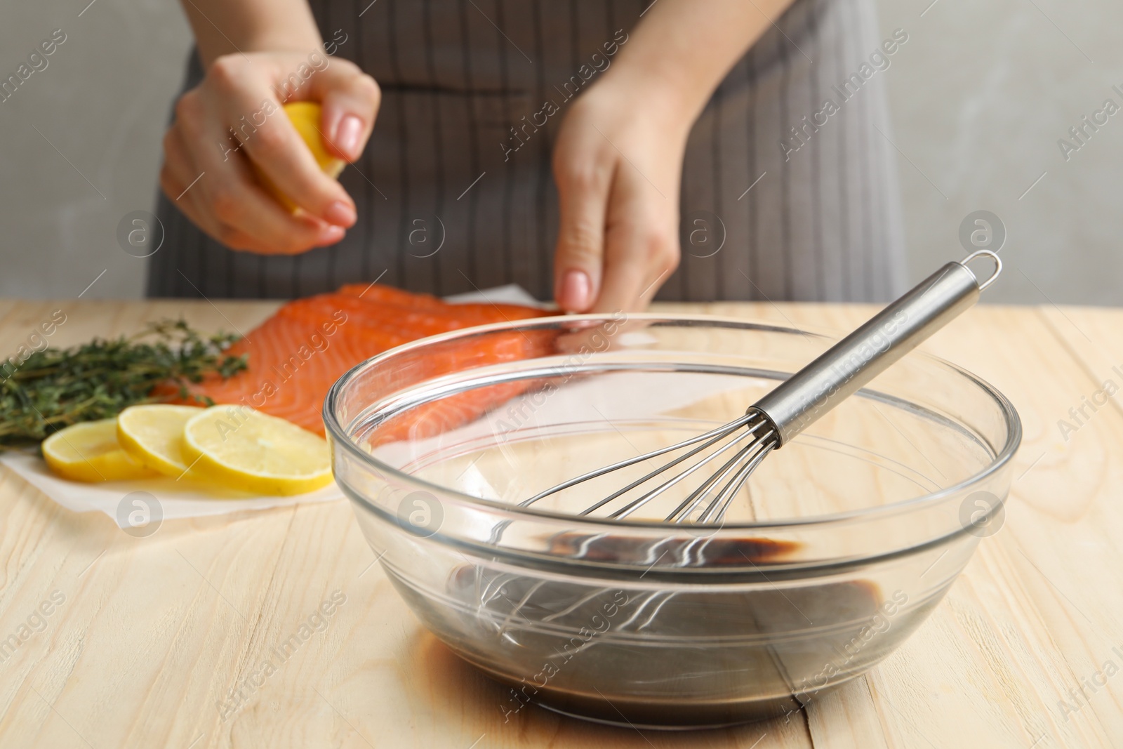 Photo of Woman squeezing lemon juice onto salmon fillet wooden at table, focus on bowl with soy sauce