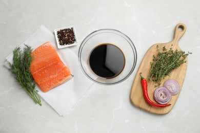 Photo of Soy sauce in bowl, salmon fillet and spices on gray marble table, flat lay