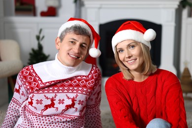 Photo of Lovely couple in Santa hats and Christmas sweaters at home