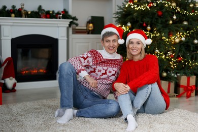 Photo of Lovely couple in Santa hats and Christmas sweaters at home