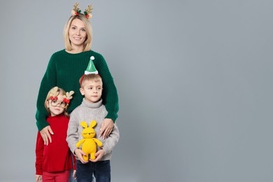 Photo of Mom with her little children in sweaters and Christmas accessories on grey background