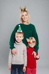 Mom with her little children in sweaters and Christmas accessories on grey background