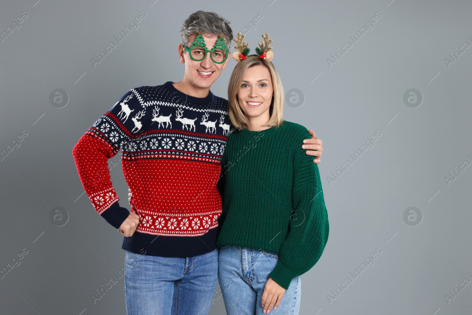 Photo of Lovely couple in Christmas sweaters and accessories on grey background