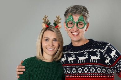 Photo of Lovely couple in Christmas sweaters and accessories on grey background