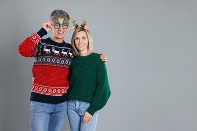 Photo of Lovely couple in Christmas sweaters and accessories on grey background. Space for text