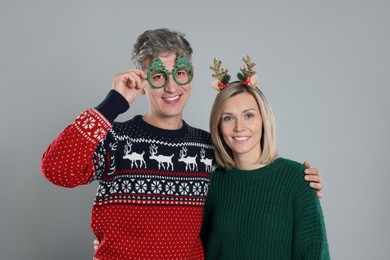 Photo of Lovely couple in Christmas sweaters and accessories on grey background