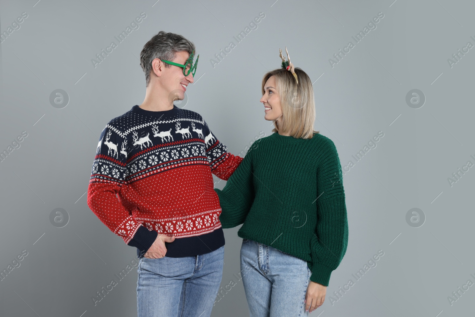 Photo of Lovely couple in Christmas sweaters and accessories on grey background