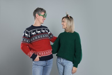 Photo of Lovely couple in Christmas sweaters and accessories on grey background