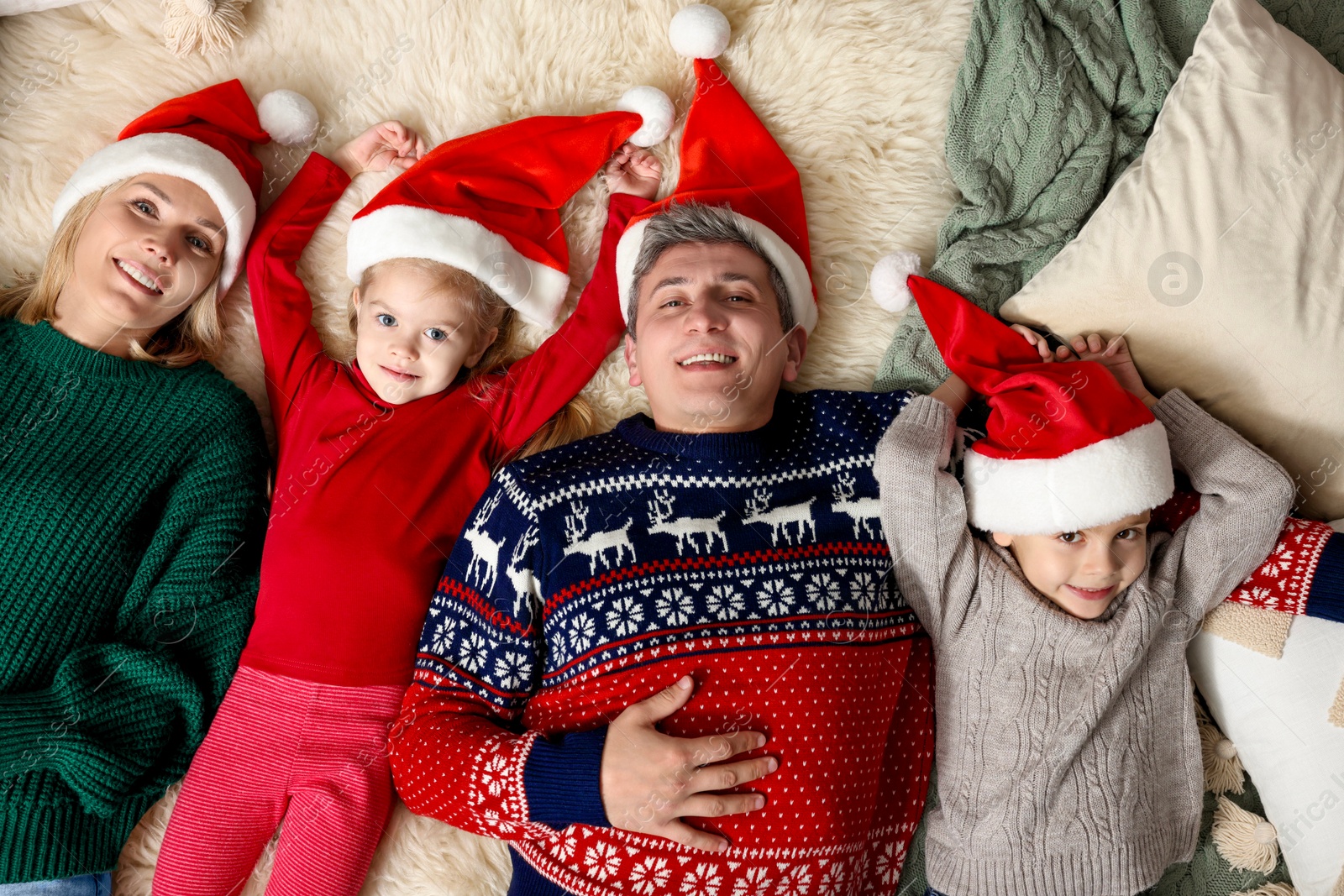 Photo of Happy family in Santa hats lying on rug together, top view. Christmas season