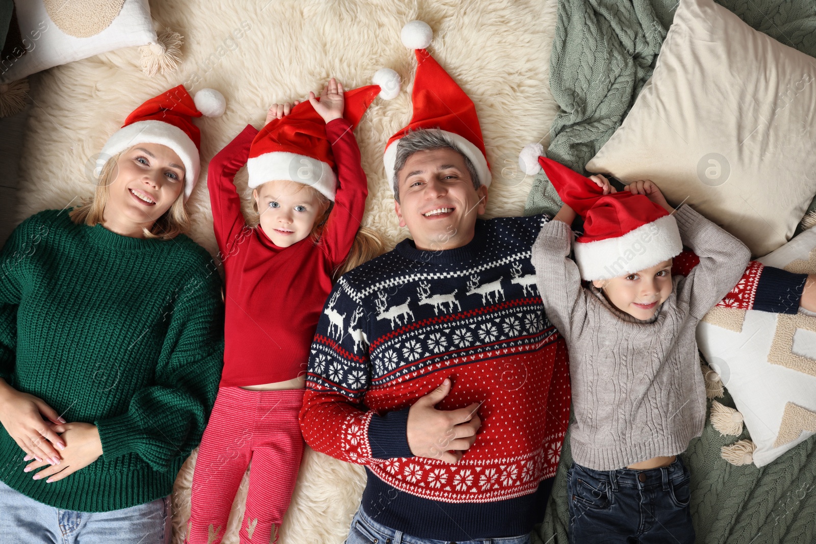 Photo of Happy family in Santa hats lying on rug together, top view. Christmas season