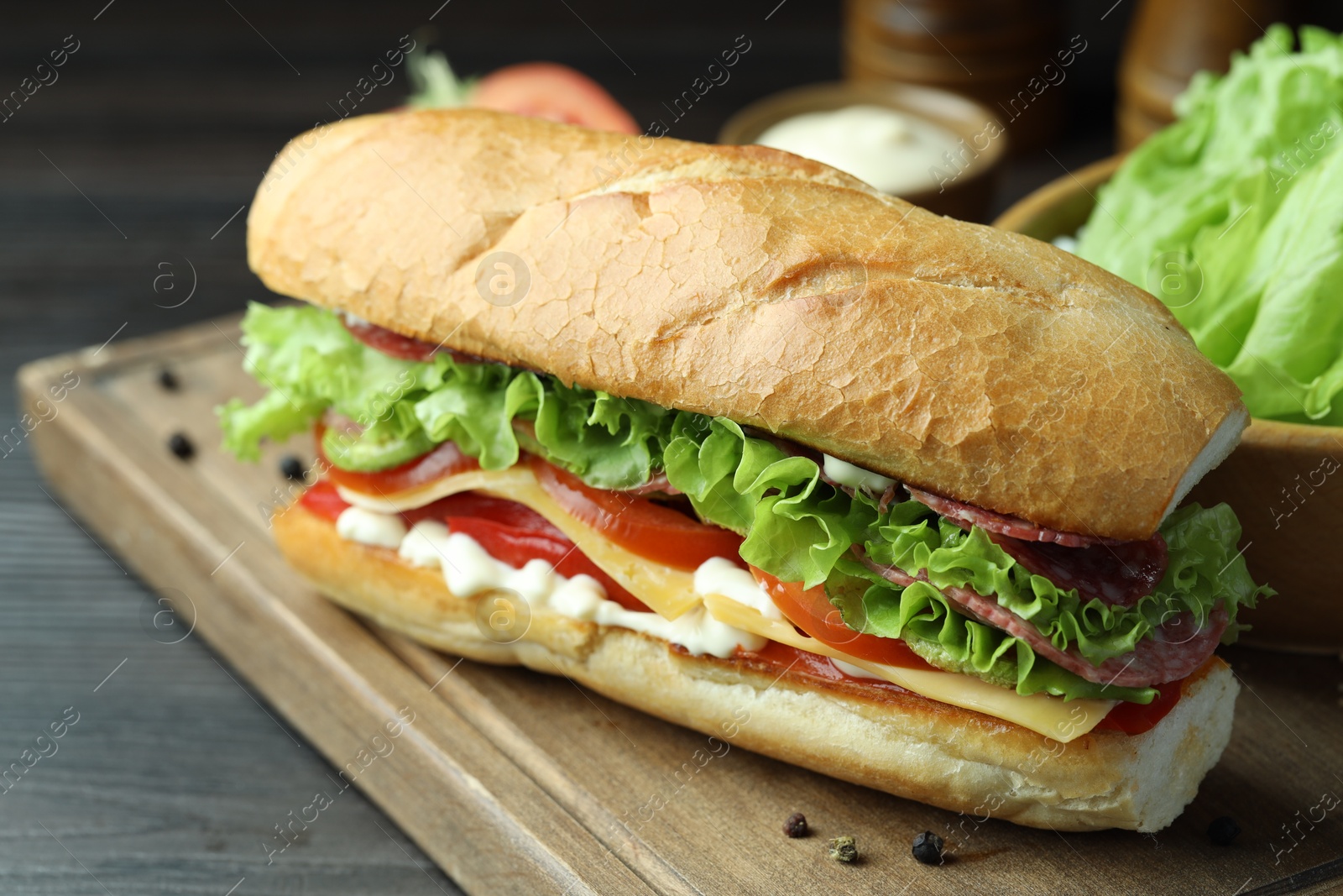 Photo of Delicious baguette sandwich with salami and cheese on grey wooden table, closeup