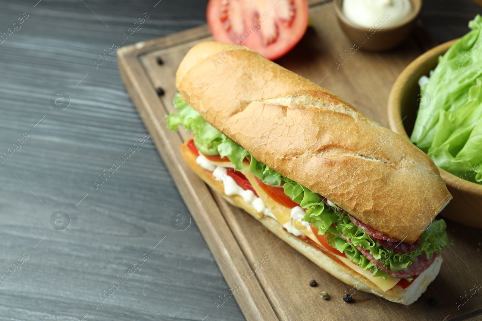 Photo of Delicious baguette sandwich with salami and cheese on grey wooden table. Space for text