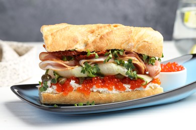 Photo of Delicious baguette sandwich with caviar, ham and capers on white wooden table, closeup