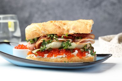 Photo of Delicious baguette sandwich with caviar, ham and capers on white wooden table, closeup