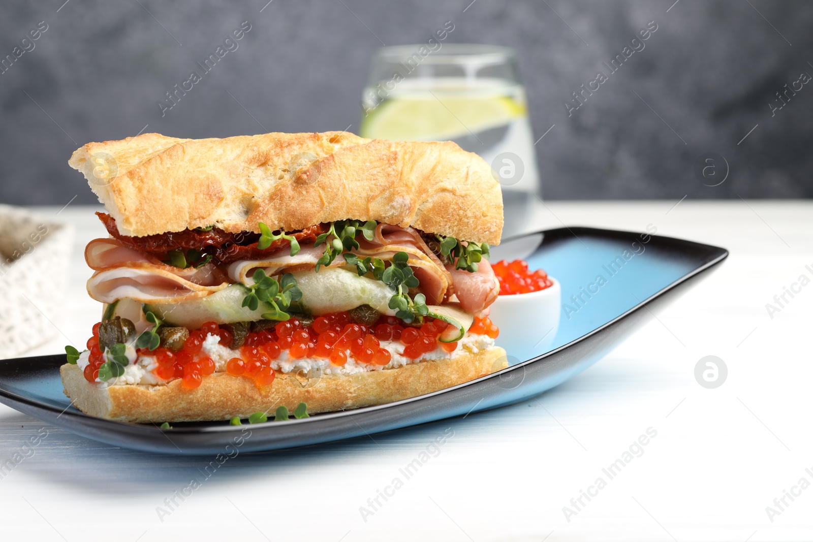 Photo of Delicious baguette sandwich with caviar, ham and capers on white wooden table