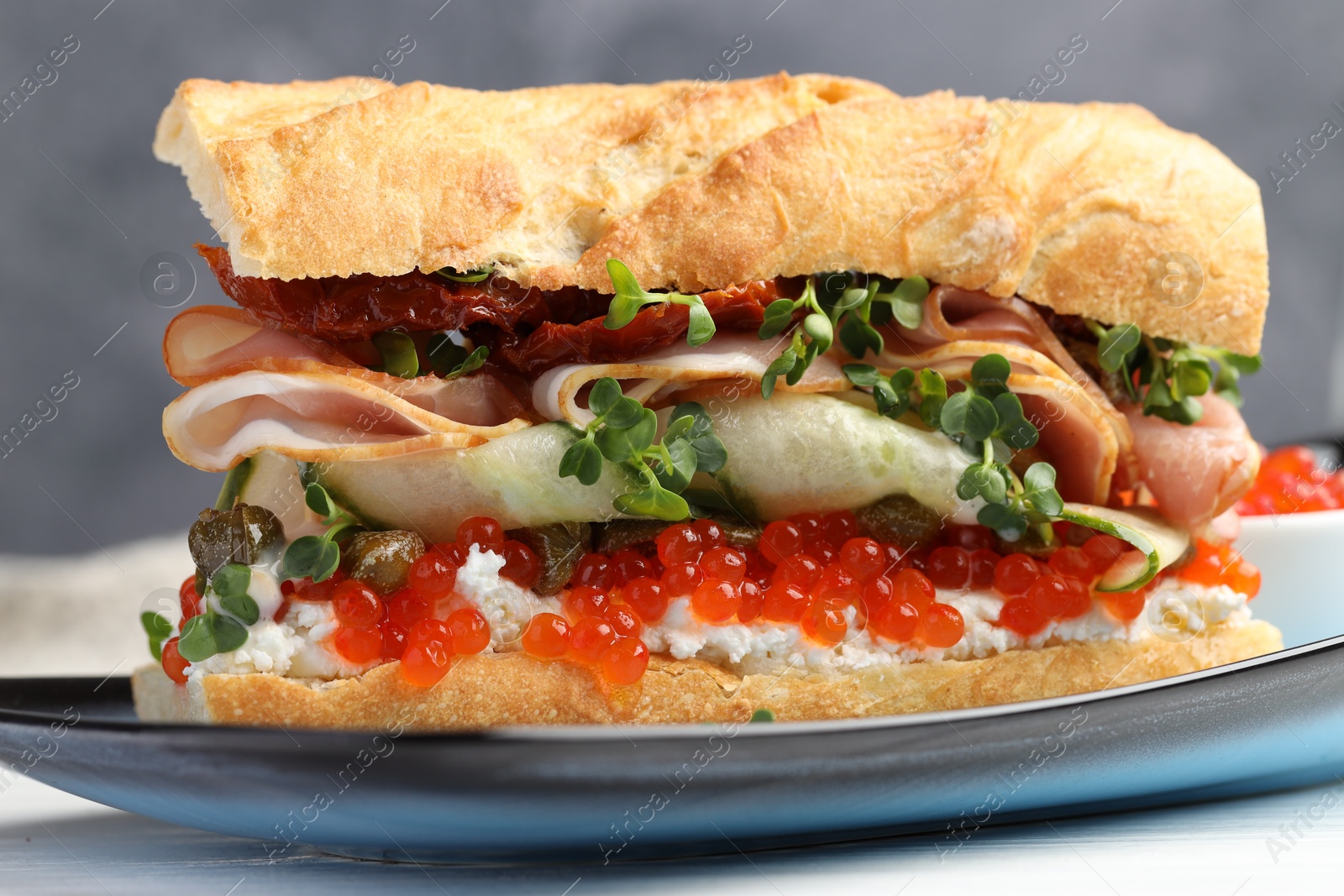 Photo of Delicious baguette sandwich with caviar, ham and capers on white wooden table, closeup