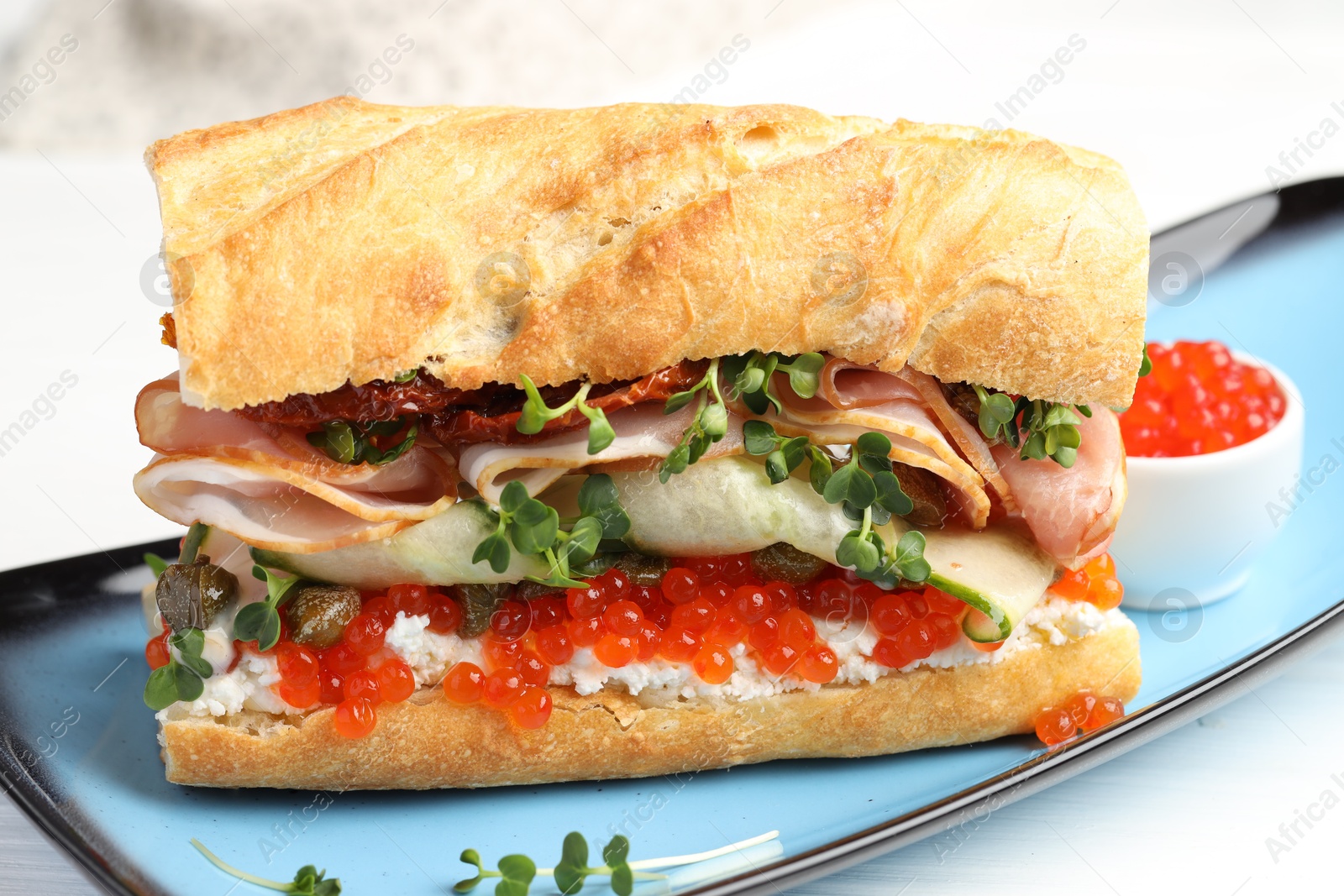 Photo of Delicious baguette sandwich with caviar, ham and capers on white wooden table, closeup