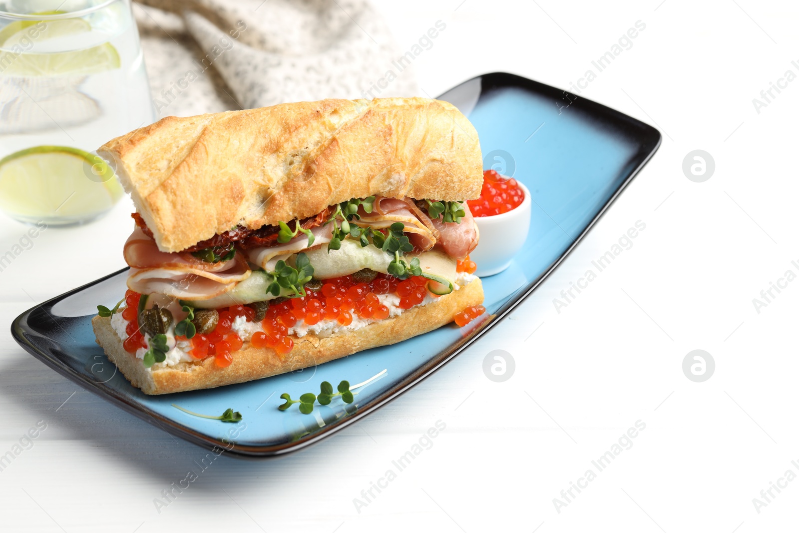 Photo of Delicious baguette sandwich with caviar, ham and capers on white wooden table, space for text