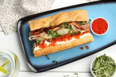 Photo of Delicious baguette sandwich with caviar, ham and capers on white wooden table, flat lay