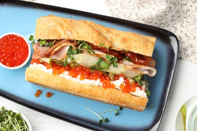 Photo of Delicious baguette sandwich with caviar, ham and capers on white wooden table, flat lay