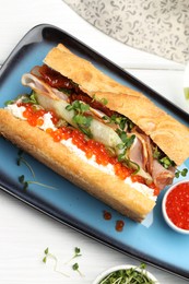 Photo of Delicious baguette sandwich with caviar, ham and capers on white wooden table, top view