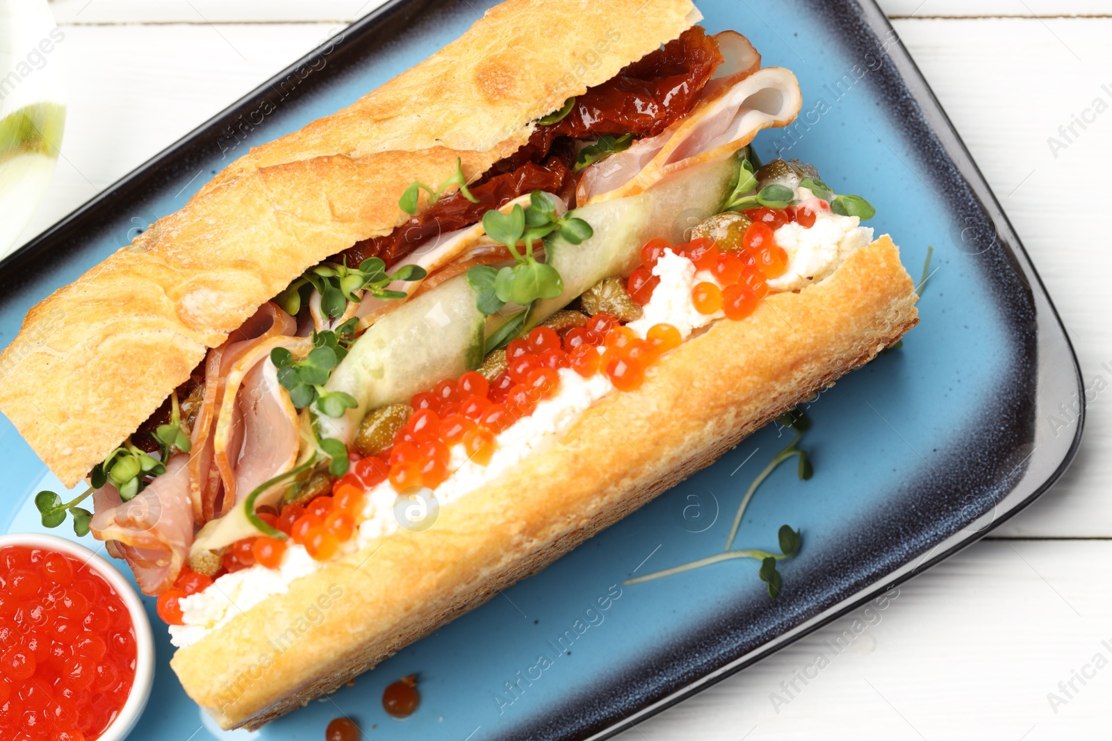 Photo of Delicious baguette sandwich with caviar, ham and capers on white wooden table, top view