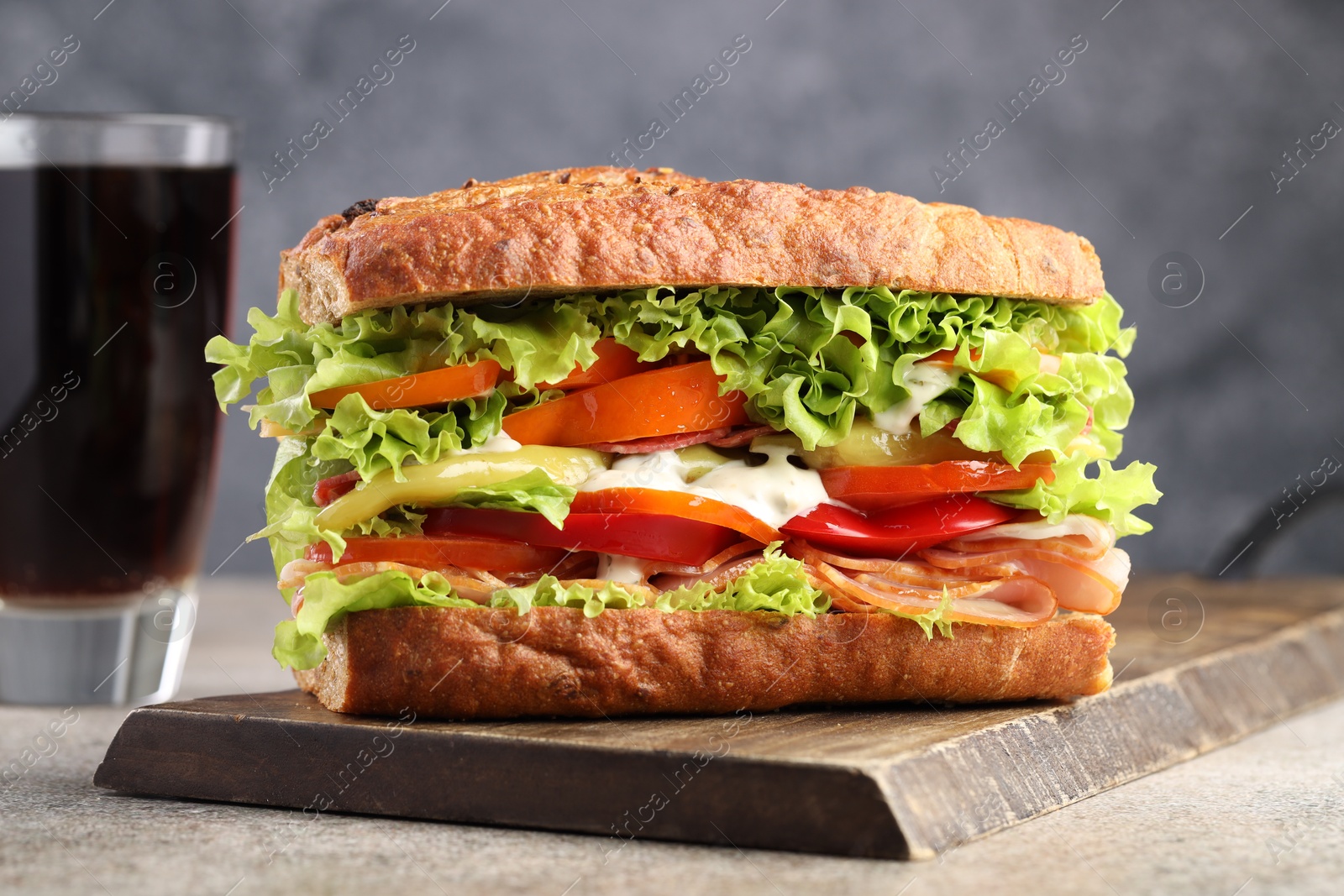 Photo of Delicious baguette sandwich with tomatoes and yellow beans on grey textured table, closeup