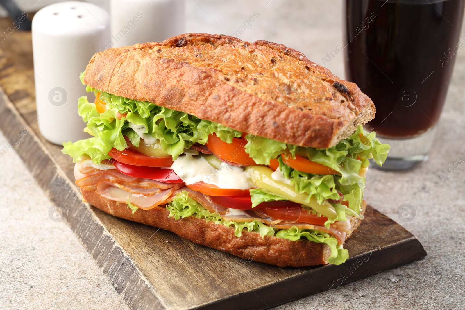 Photo of Delicious baguette sandwich with tomatoes and yellow beans on grey textured table, closeup