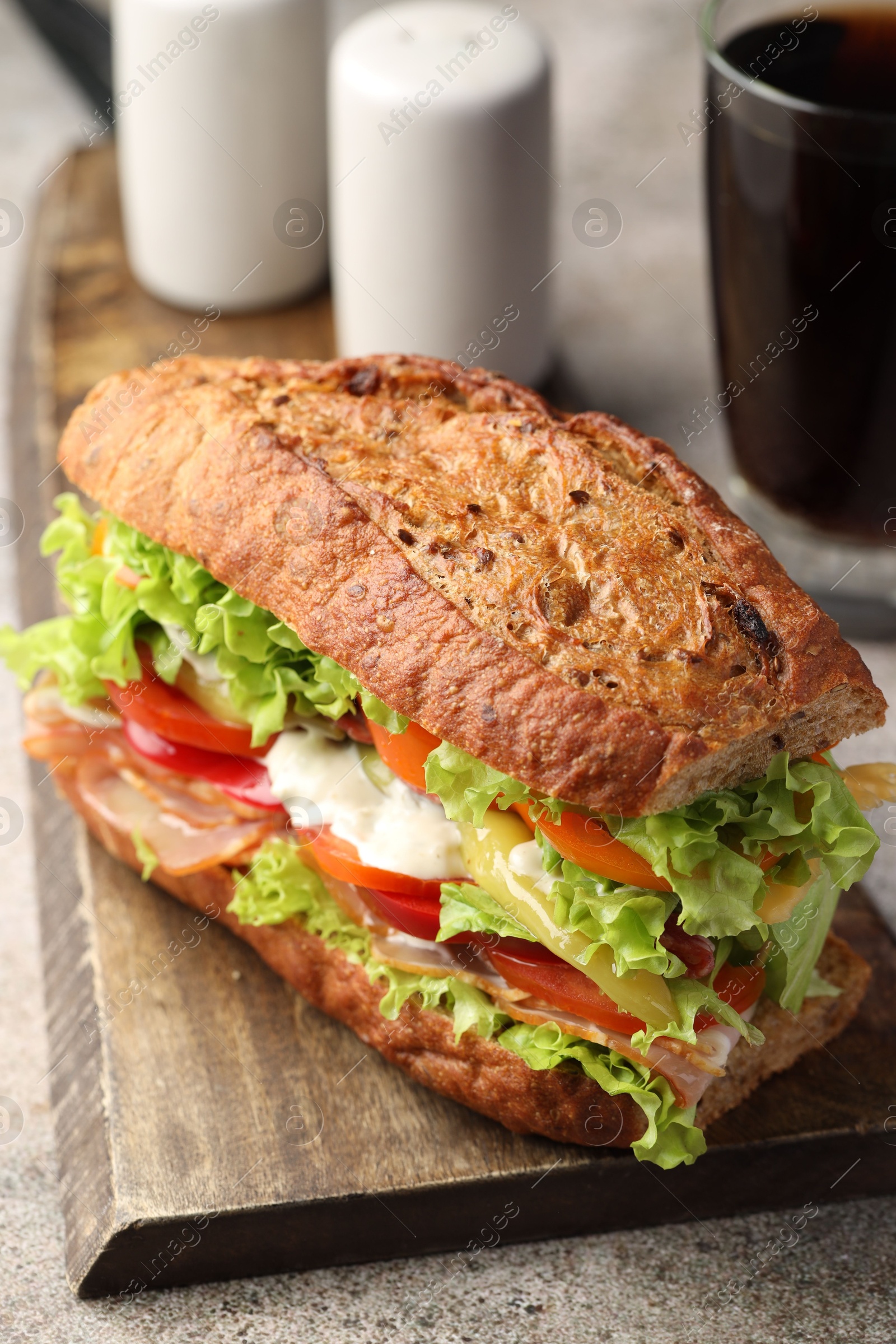 Photo of Delicious baguette sandwich with tomatoes and yellow beans on grey textured table, closeup