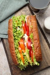 Photo of Delicious baguette sandwich with tomatoes and yellow beans on grey textured table, top view