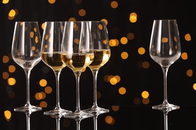 Photo of Tasty white wine in glasses on mirror surface against dark background with blurred lights. Bokeh effect