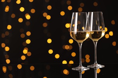 Photo of Tasty white wine in glasses on mirror surface against dark background with blurred lights, space for text. Bokeh effect