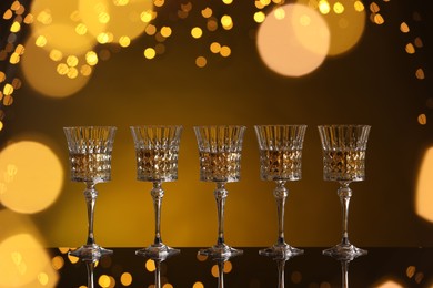 Photo of Tasty white wine in glasses on mirror surface against golden background with blurred lights. Bokeh effect