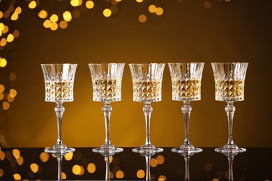 Photo of Tasty white wine in glasses on mirror surface against golden background with blurred lights. Bokeh effect