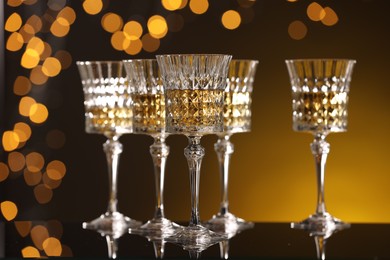 Photo of Tasty white wine in glasses on mirror surface against golden background with blurred lights. Bokeh effect