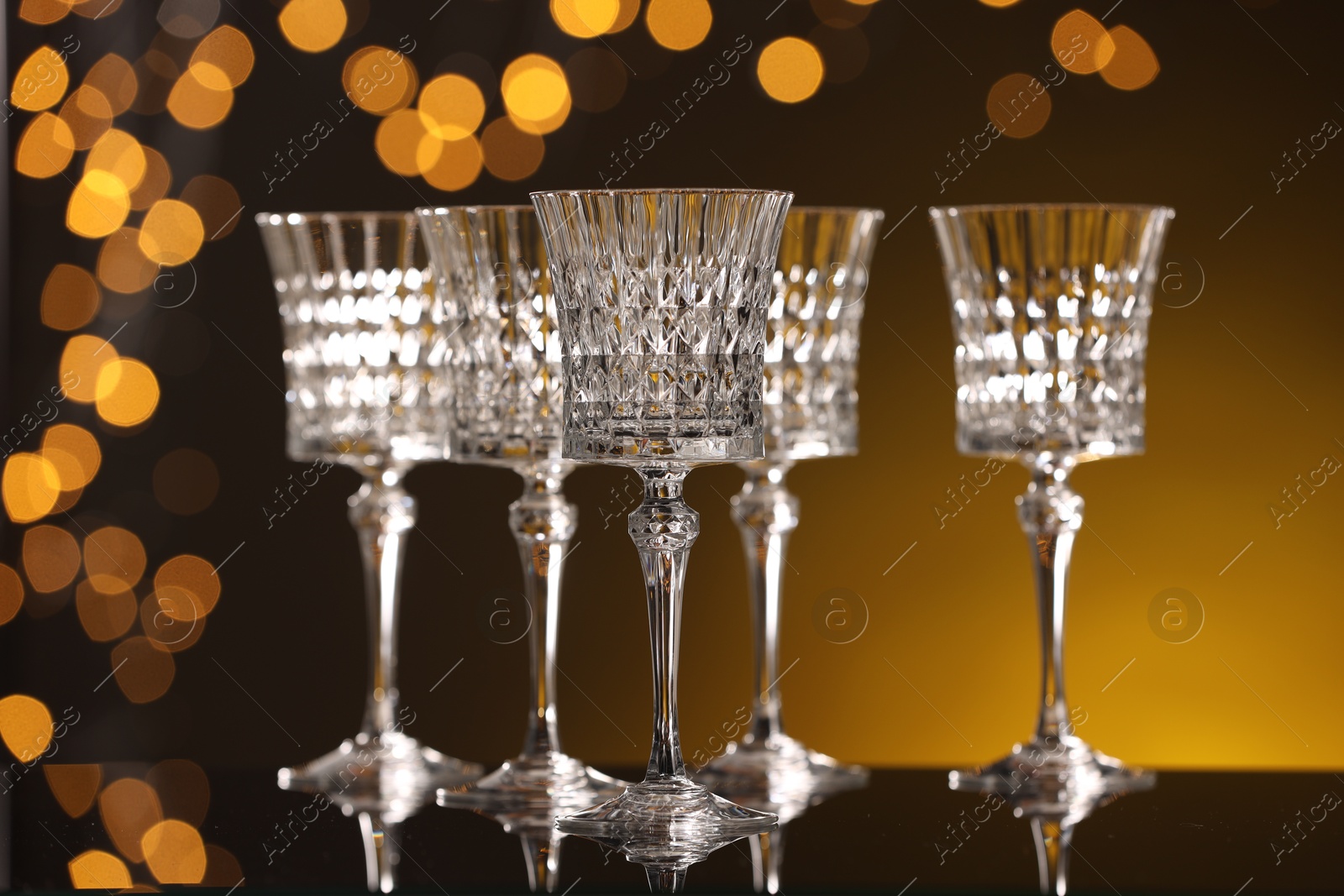 Photo of Empty wineglasses on mirror surface against golden background with blurred lights, bokeh effect