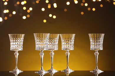 Photo of Empty wineglasses on mirror surface against golden background with blurred lights, bokeh effect