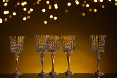 Photo of Empty wineglasses on mirror surface against golden background with blurred lights, bokeh effect