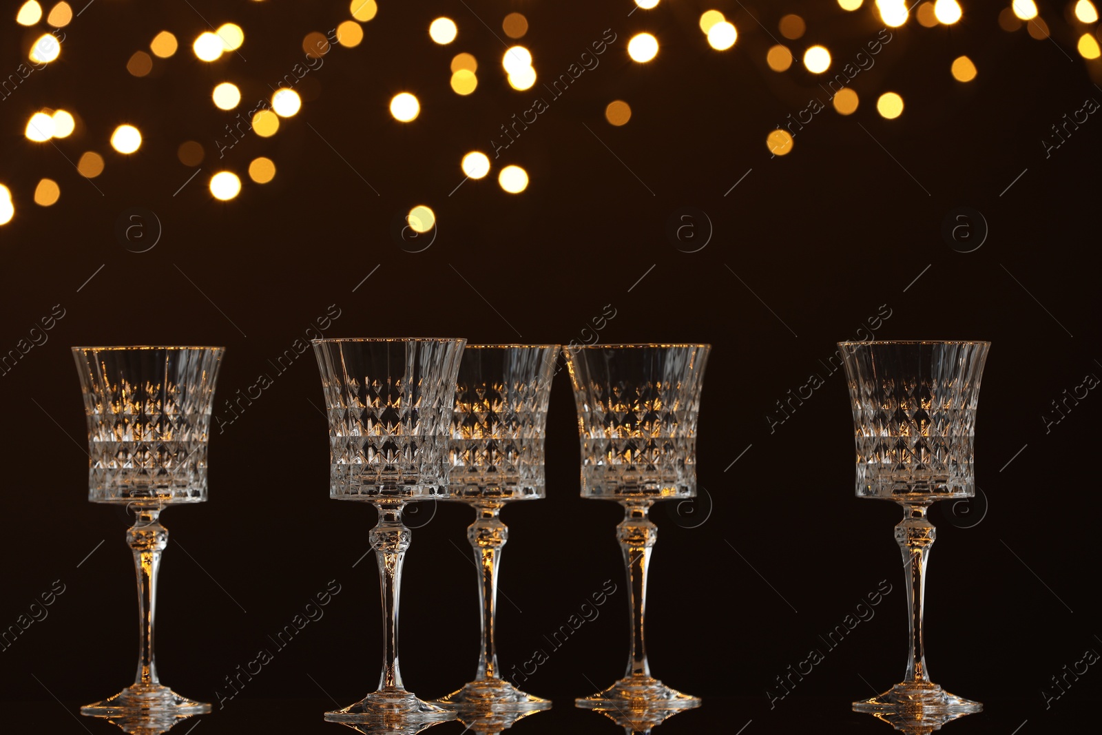 Photo of Empty wineglasses on mirror surface against dark background with blurred lights. Bokeh effect