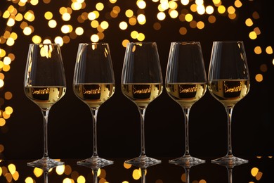 Photo of Tasty white wine in glasses on mirror surface against dark background with blurred lights. Bokeh effect