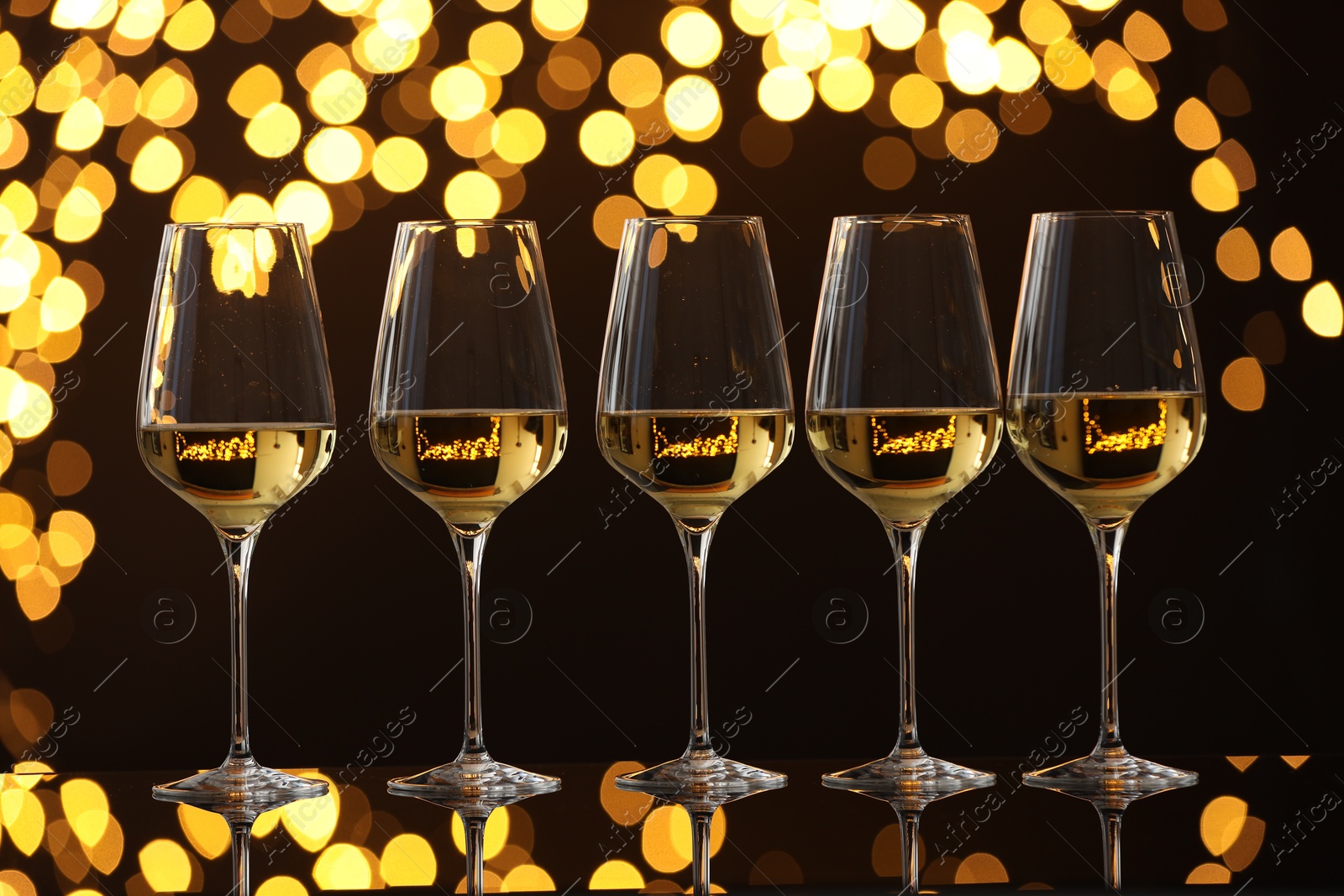 Photo of Tasty white wine in glasses on mirror surface against dark background with blurred lights. Bokeh effect