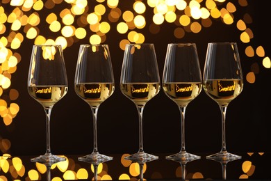 Photo of Tasty white wine in glasses on mirror surface against dark background with blurred lights. Bokeh effect