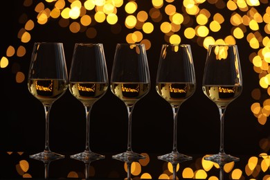 Photo of Tasty white wine in glasses on mirror surface against dark background with blurred lights. Bokeh effect